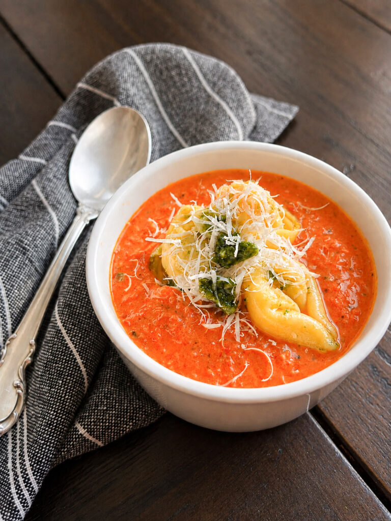 Creamy tomato tortellini soup topped with cheese tortellini, freshly grated Parmesan, and pesto.