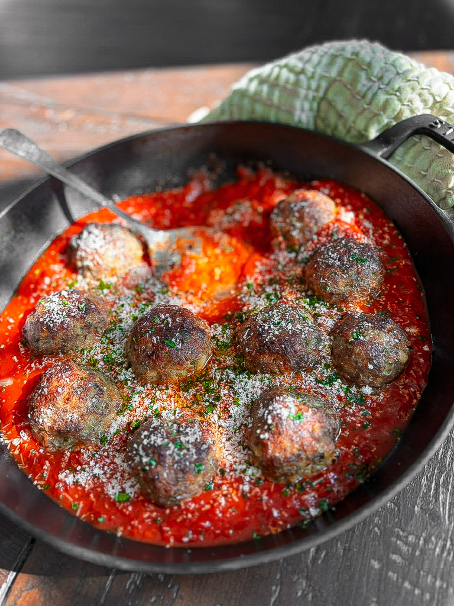 Oven baked meatballs simmering in marinara sauce in a black skillet with parmesan and herbs