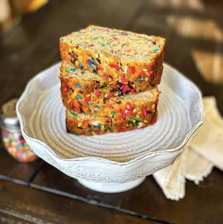 Thick slices of confetti banana bread on a glass pedestal plate.