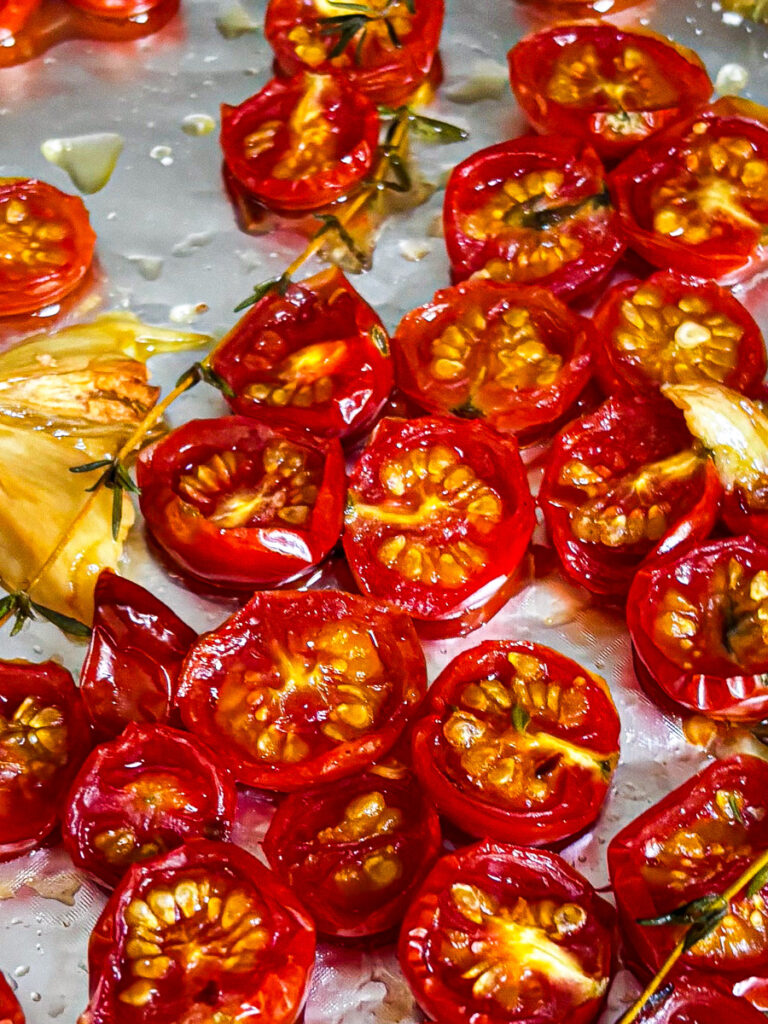 Roasted cherry tomatoes on a baking sheet with olive oil and herbs.