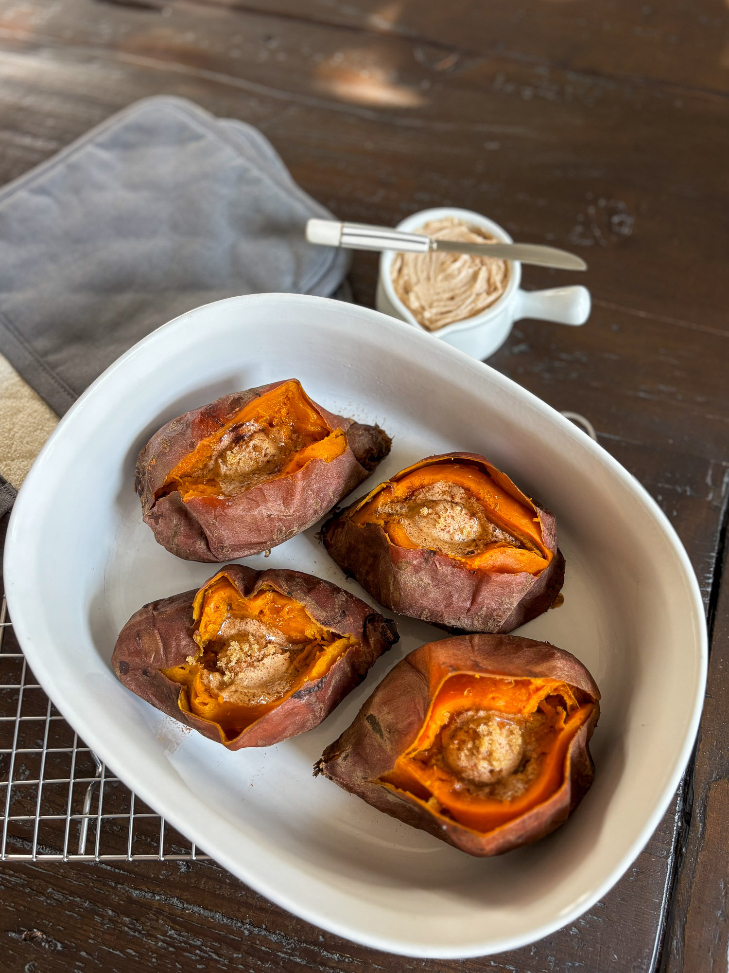 Baked Sweet Potatoes with Harvest Honey Butter-2 Four baked sweet potatoes topped with butter and cinnamon in a white dish