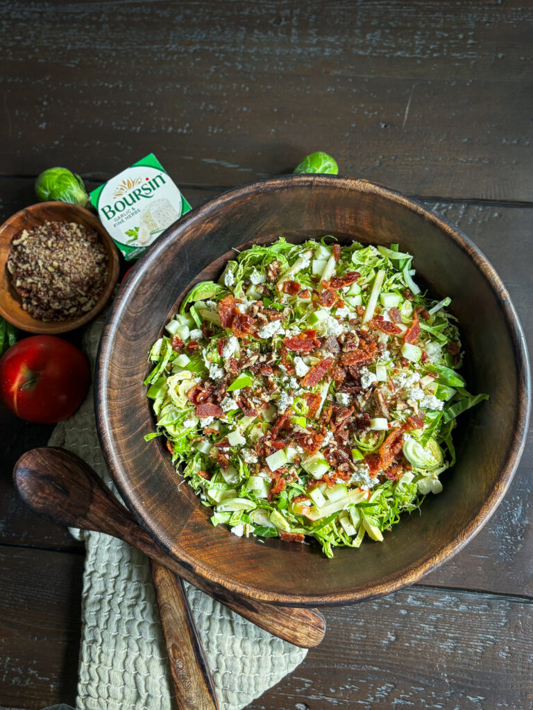 Brussels sprouts salad with apples, Boursin cheese, bacon and pecans in a wooden serving bowl