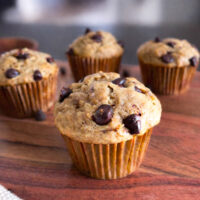 Homemade banana chocolate chip muffin with chocolate chips on top, served on a wooden board.