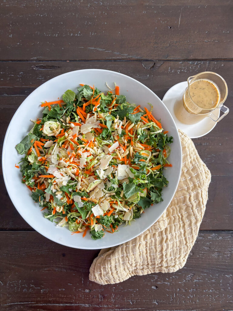 Brussels sprouts salad with kale and carrots in a white bowl with honey vinaigrette, parmesan, and almonds