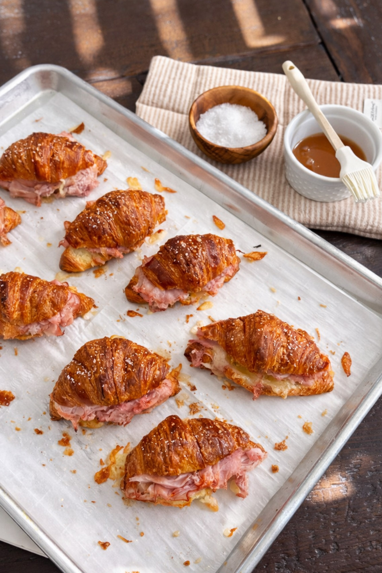 Baked Ham and Cheese Croissant Minis 2 Baked croissant sandwiches filled with ham and melted cheese on a parchment-lined baking sheet