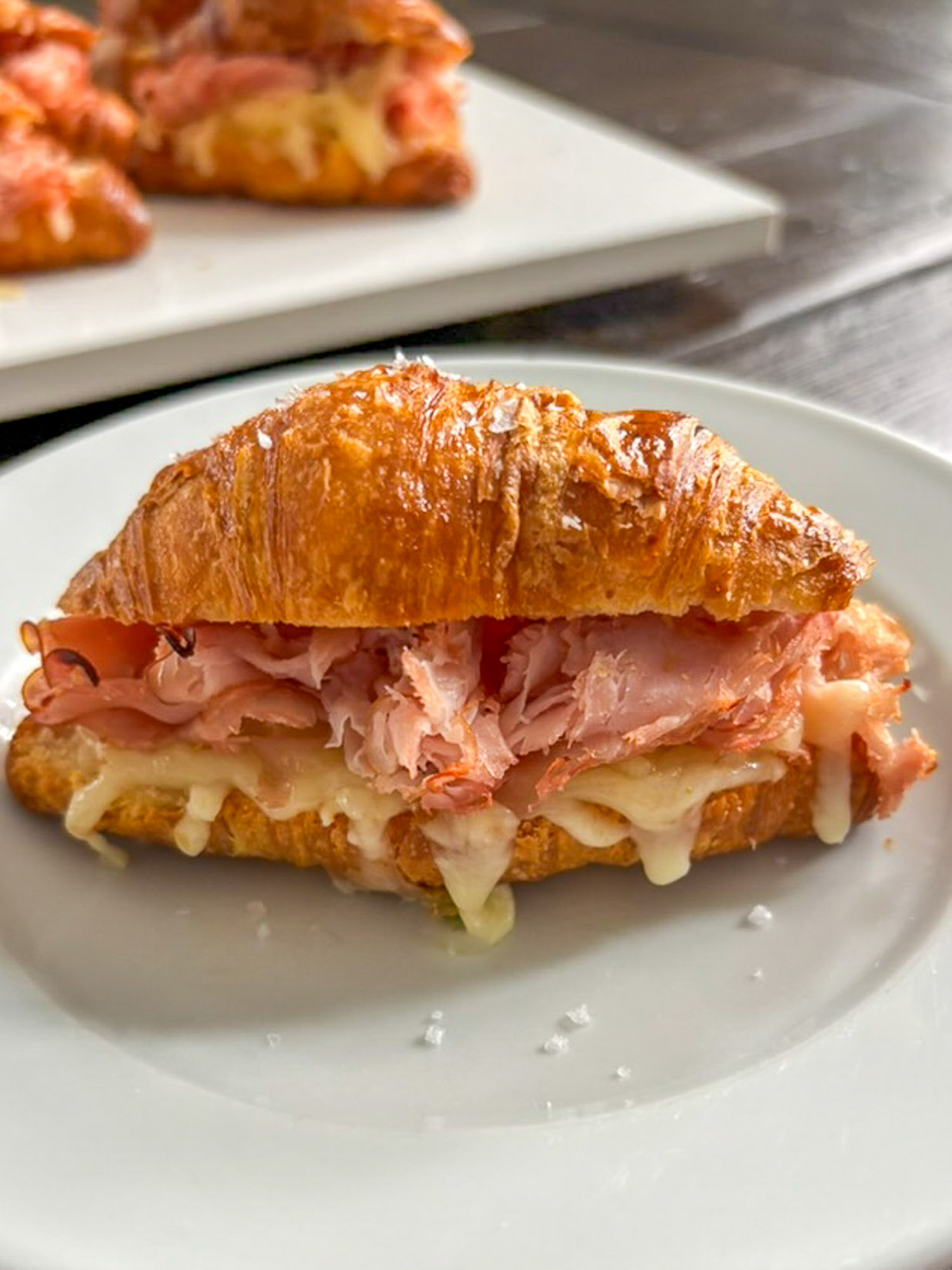 Baked Ham and Cheese Croissant Minis 3 Croissant sandwich with melted cheese and sliced ham on a white plate