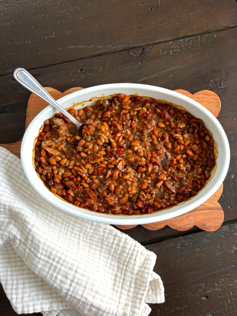 Easy baked beans with sausage and bacon baked until hot and bubbly in a white serving dish.