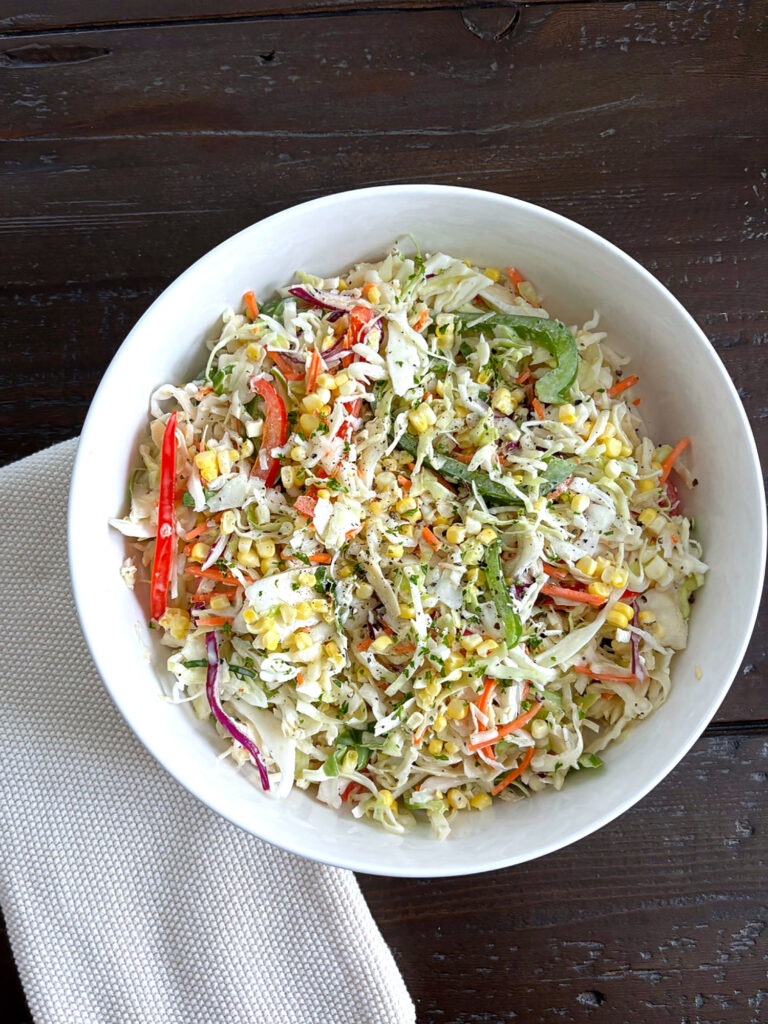 Creamy Summer Coleslaw made with cabbage, sweet corn, red and green bell peppers, and a creamy dressing served in a white bowl.