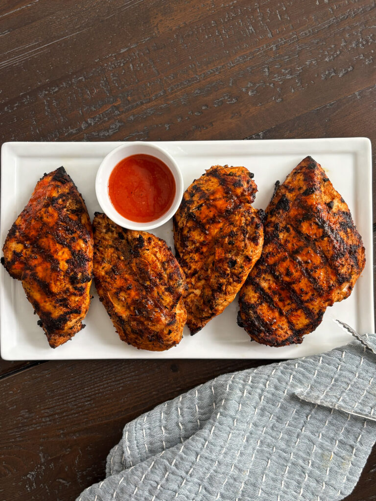 Grilled buffalo chicken breasts served on a white platter with Frank’s RedHot sauce.