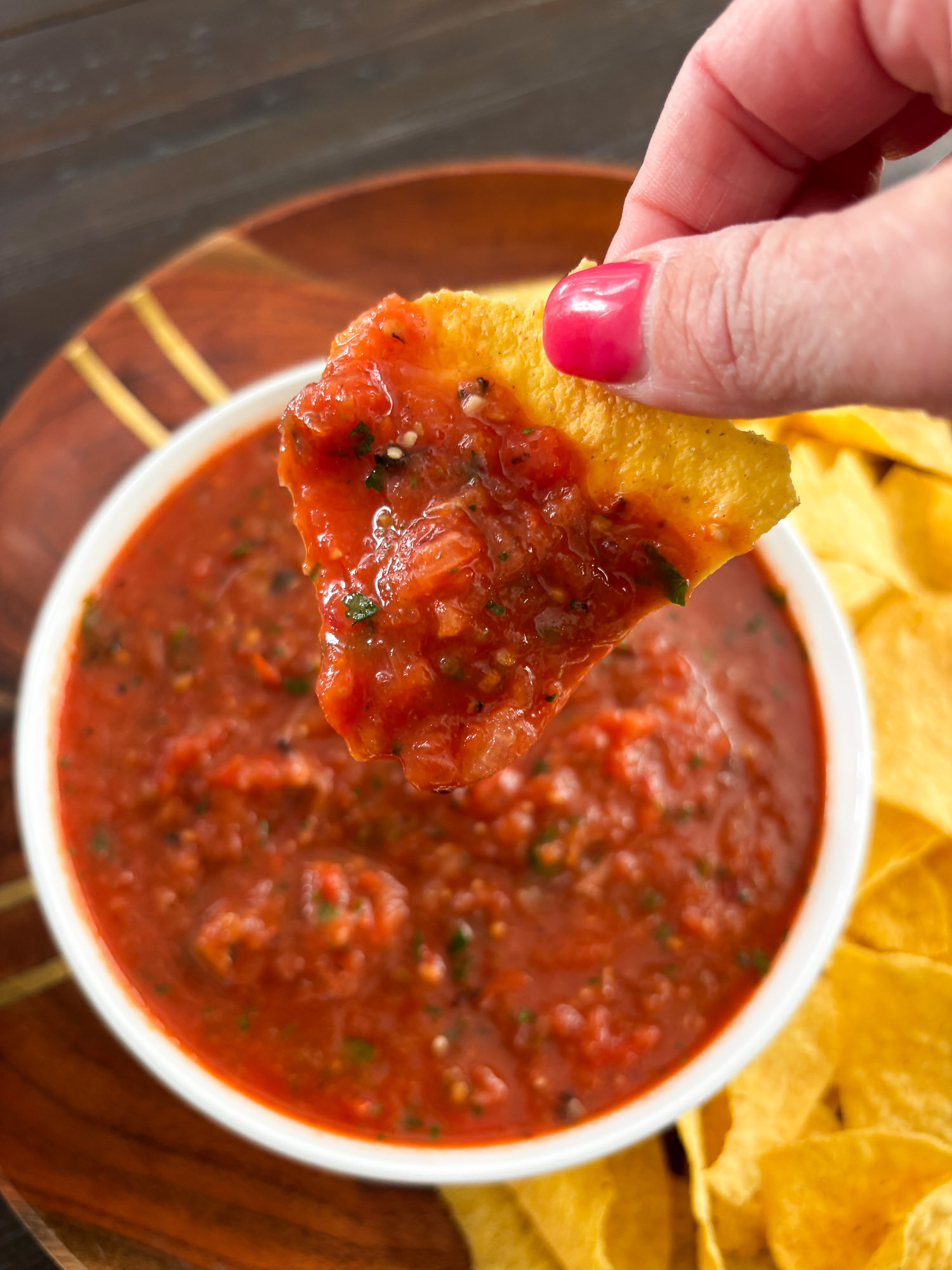 Roasted Tomato Salsa 4 Hand dipping a tortilla chip into a bowl of chunky red salsa