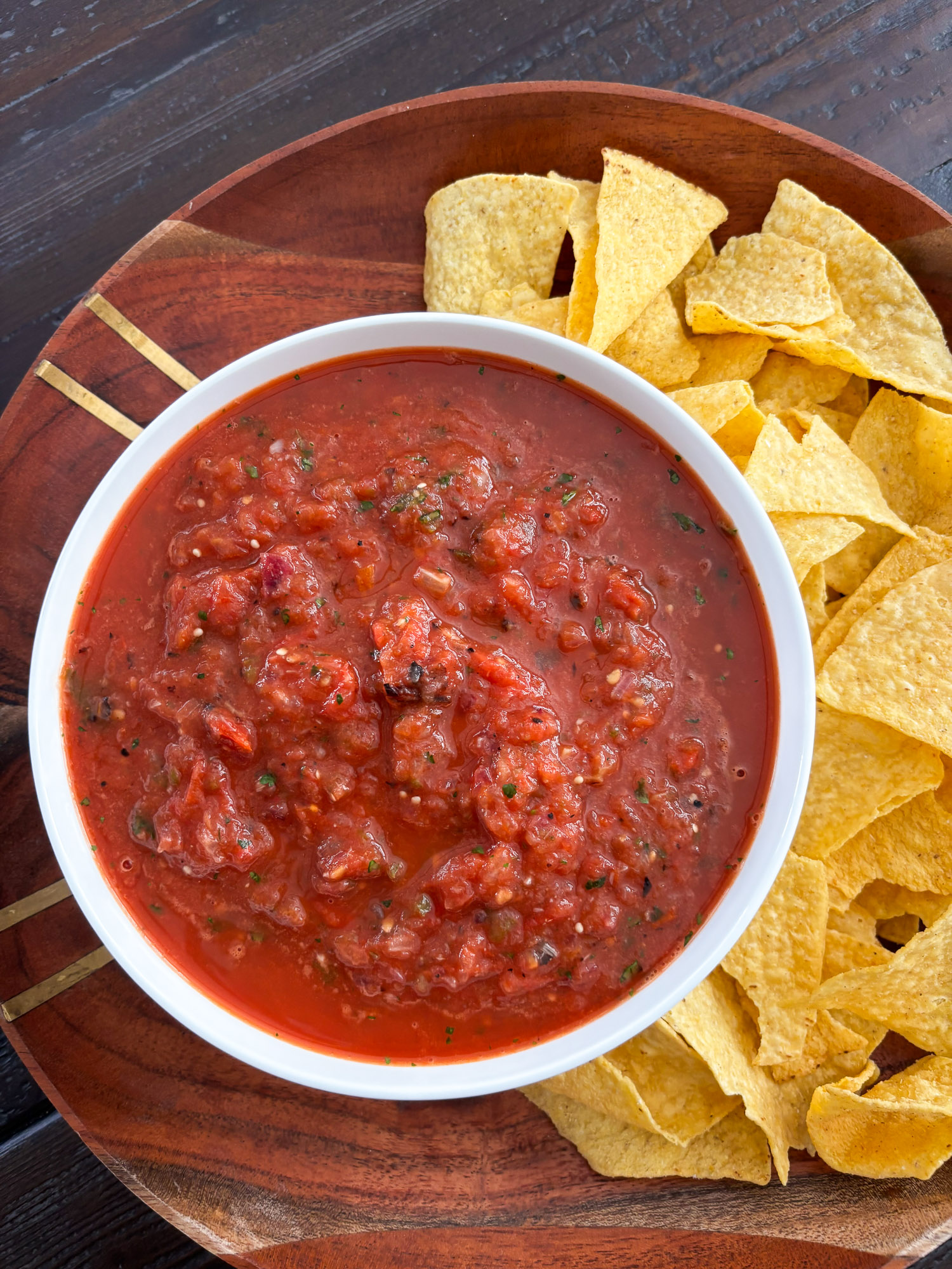 Roasted salsa in a white bowl on a wooden board with tortilla chips